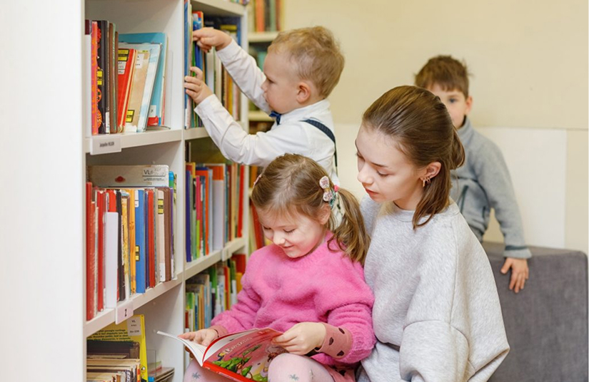 Vaikai renkasi knygas darželio bibliotekos lentynoje