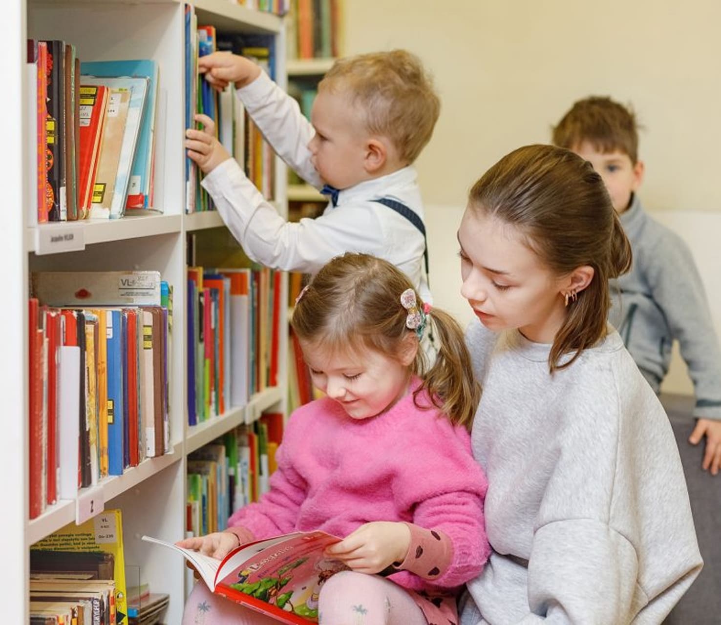 Vaikai renkasi knygas bibliotekos lentynoje