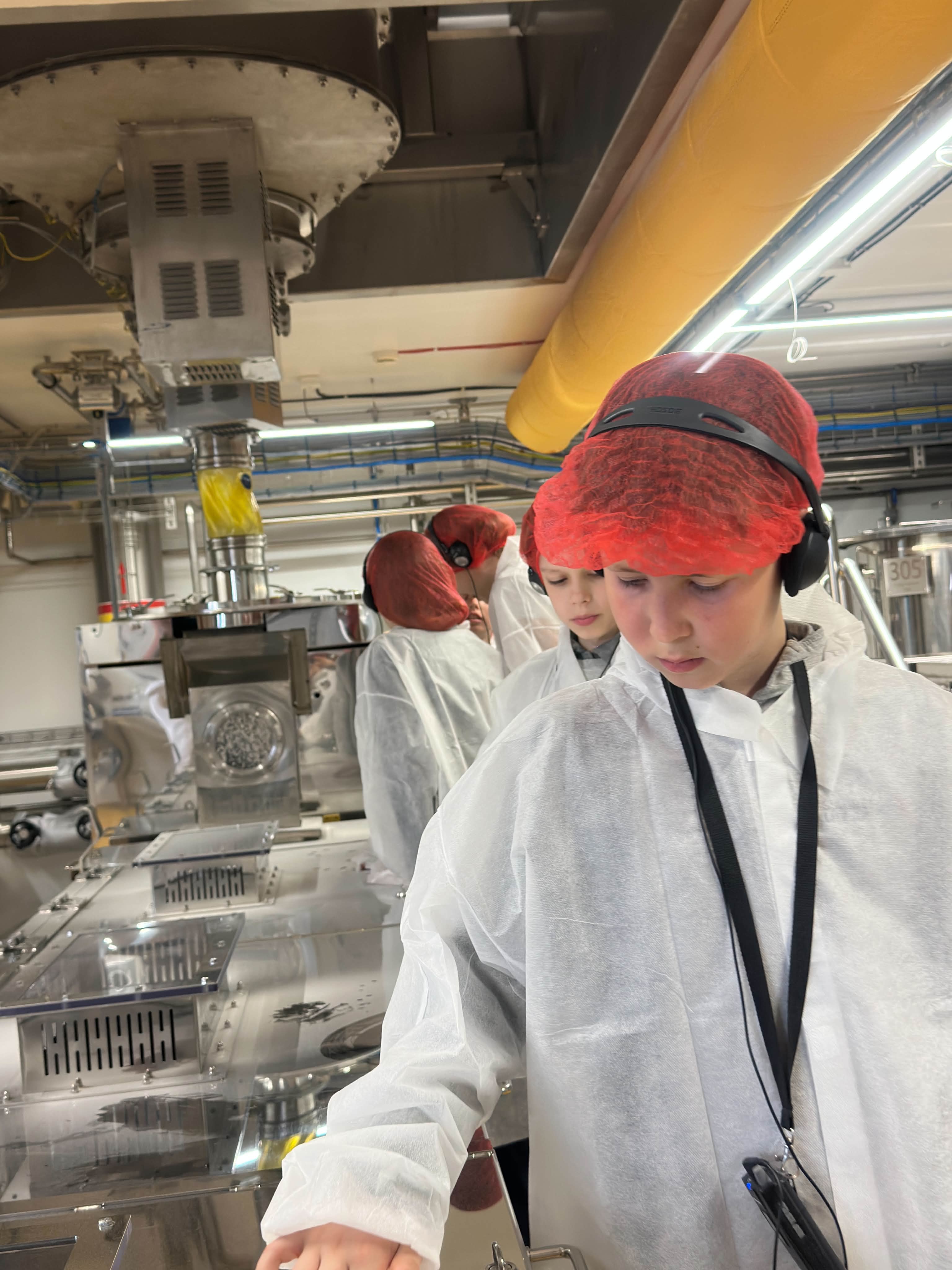 Mokiniai su apsauginiais chalatais makaronų fabrike